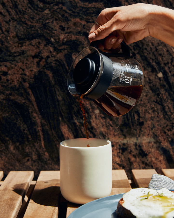 Person pouring coffee into cup on table