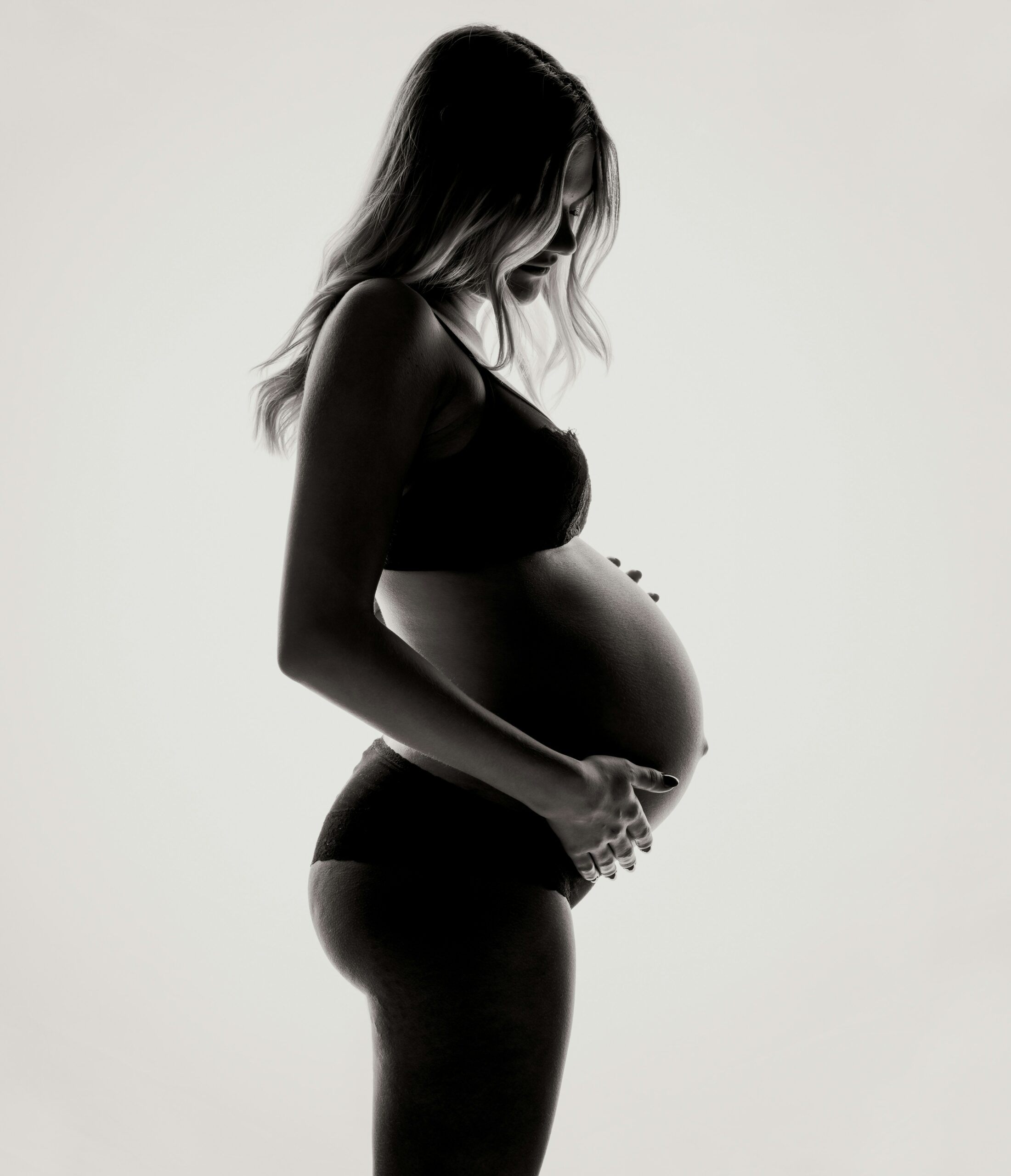 Pregnant woman wearing black underwear, standing in front of a white background